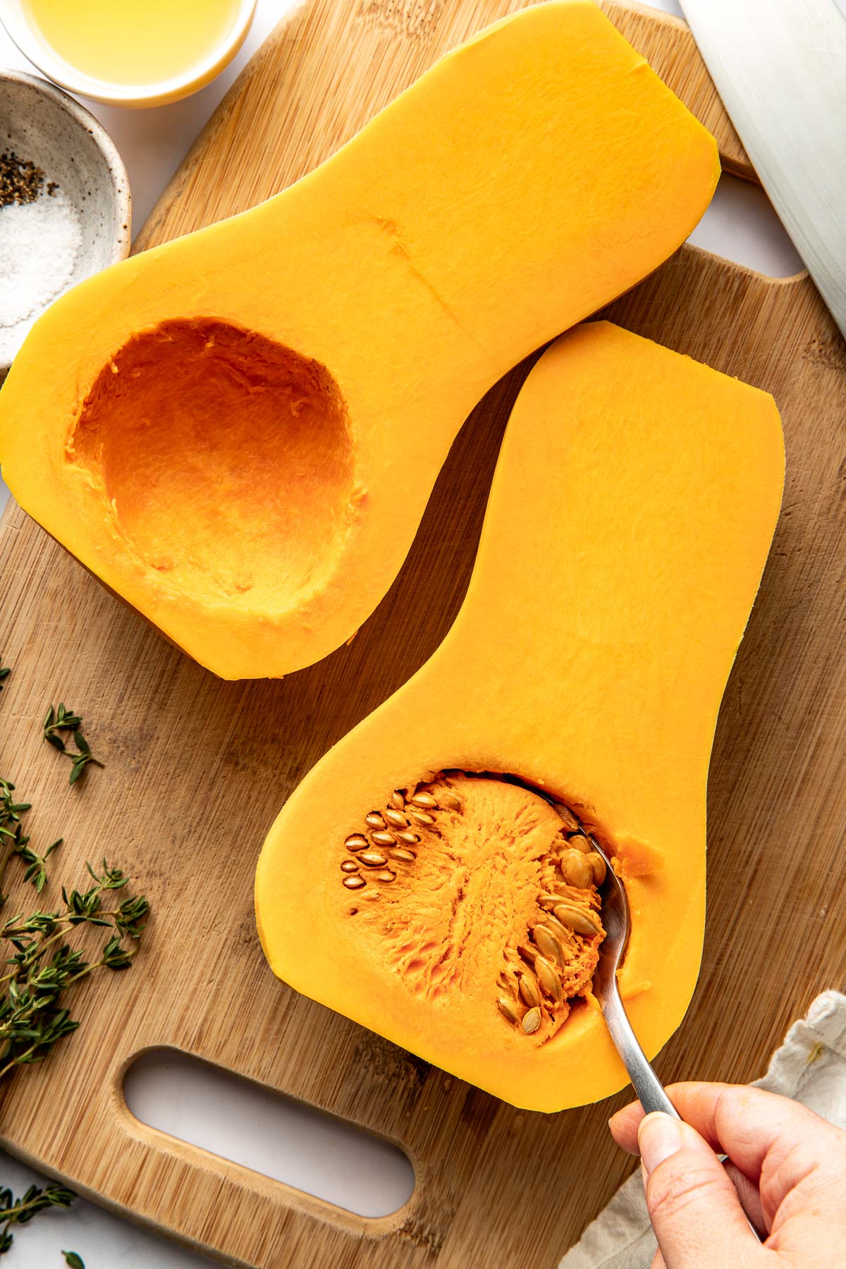 Close up view of a butternut squash cut in half and a spoon scooping out the seedy insides. 