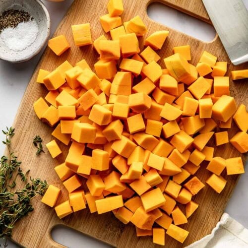 Overhead view of a wooden cutting board filled with cubed butternut squash pieces.