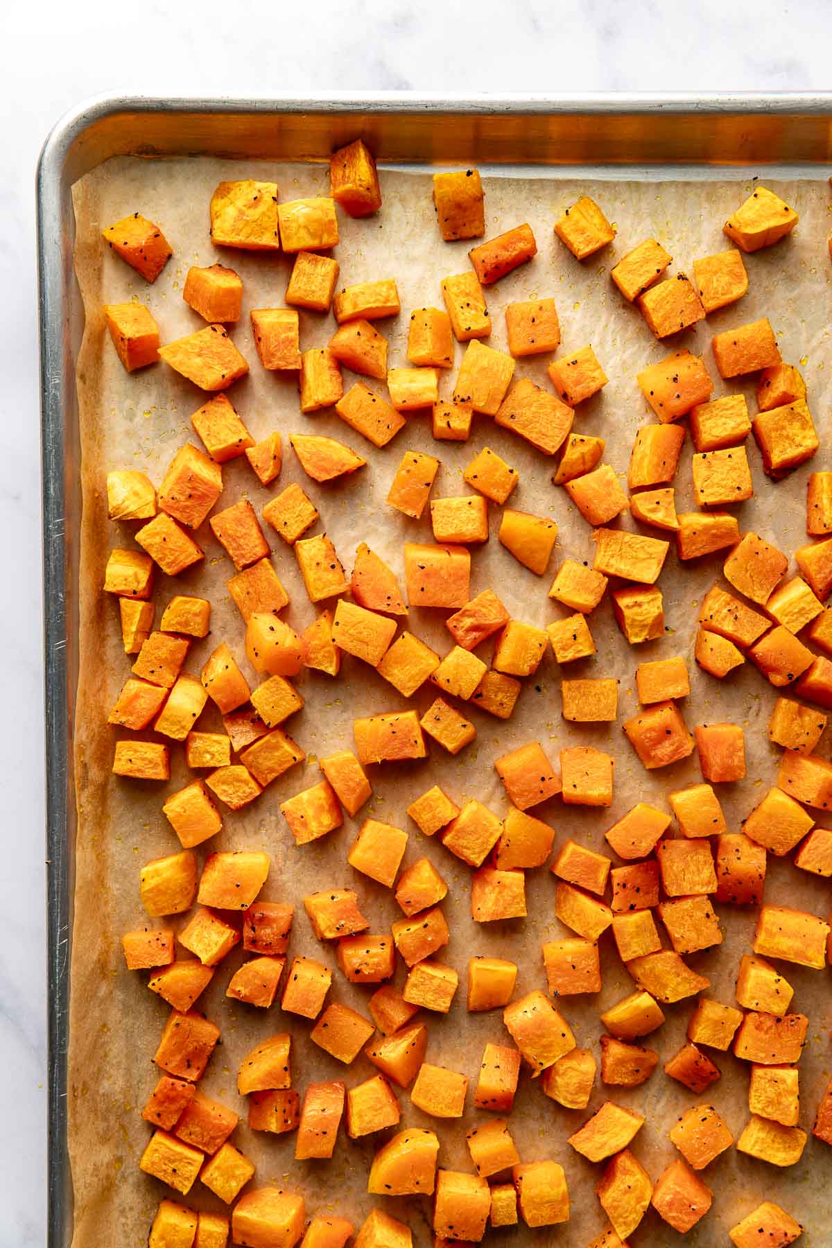 Overhead view of a sheet pan lined with parchment paper and filled with freshly roasted butternut squash cubes.