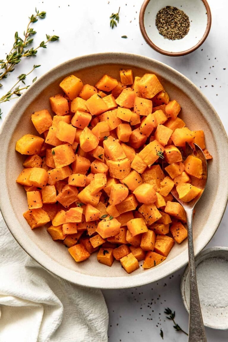 Close up view of a bowl of freshly Roasted Butternut Squash cubes perfectly crisp and seasoned with fresh herbs sprinkled on top.