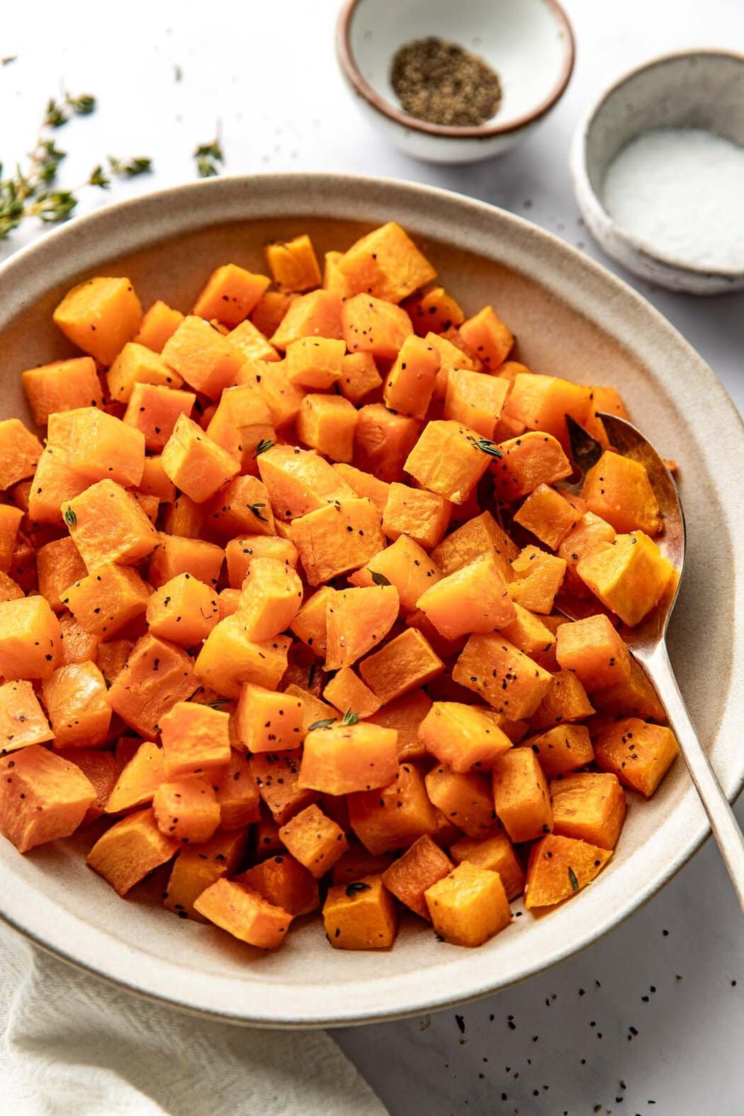 Close up view of a bowl of freshly Roasted Butternut Squash cubes perfectly crisp and seasoned with fresh herbs sprinkled on top.