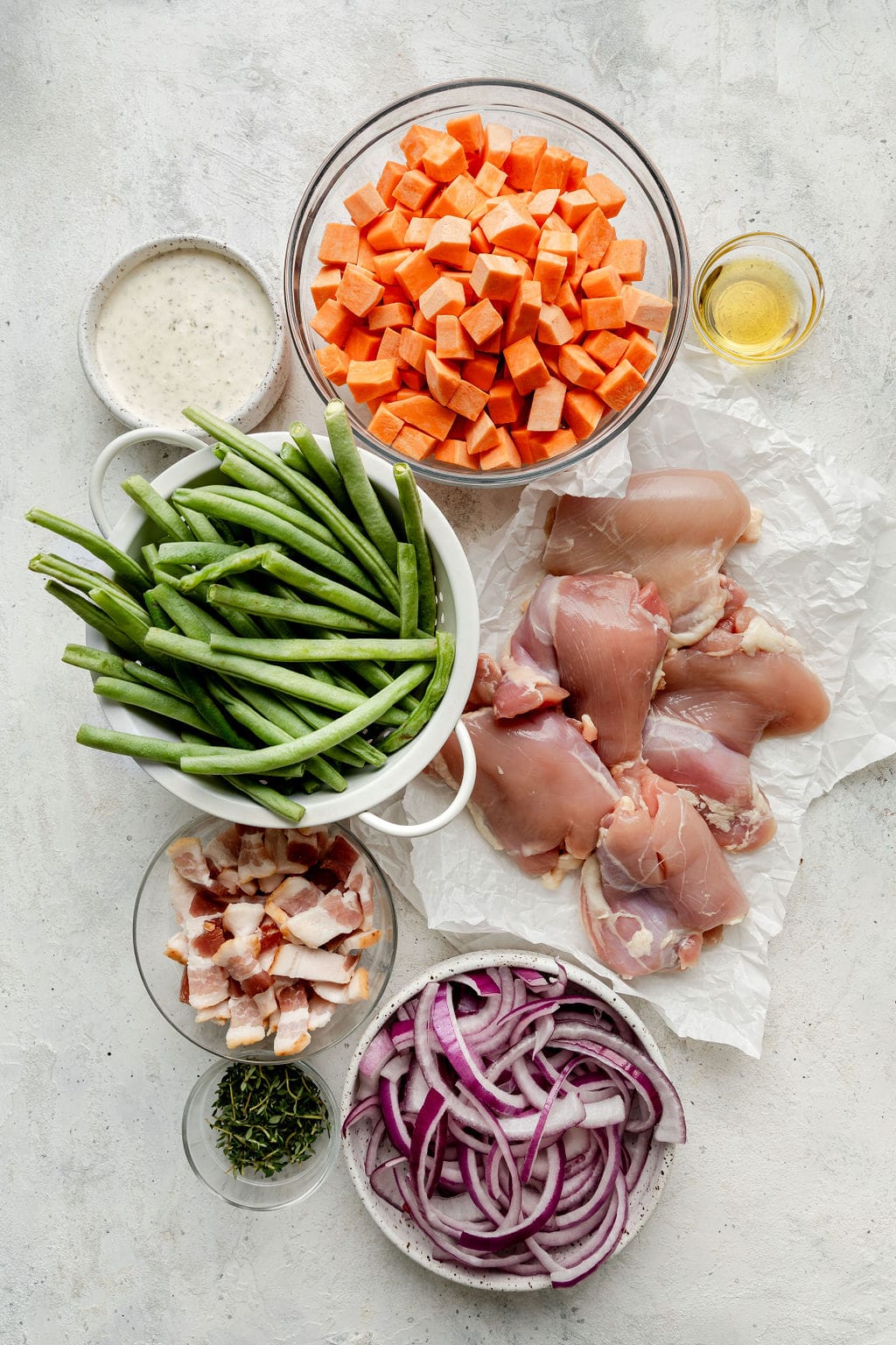 Overhead view of variety of ingredients in glass bowls for sheet pan chicken bacon ranch. 