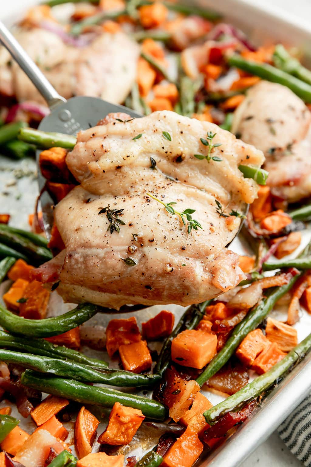 Close up view of a metal spoon scooping up a helping of chicken bacon ranch off a sheet pan. 