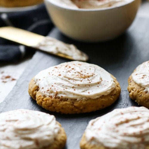 Several pumpkin cookies on a slate serving tray topped with cream cheese frosting