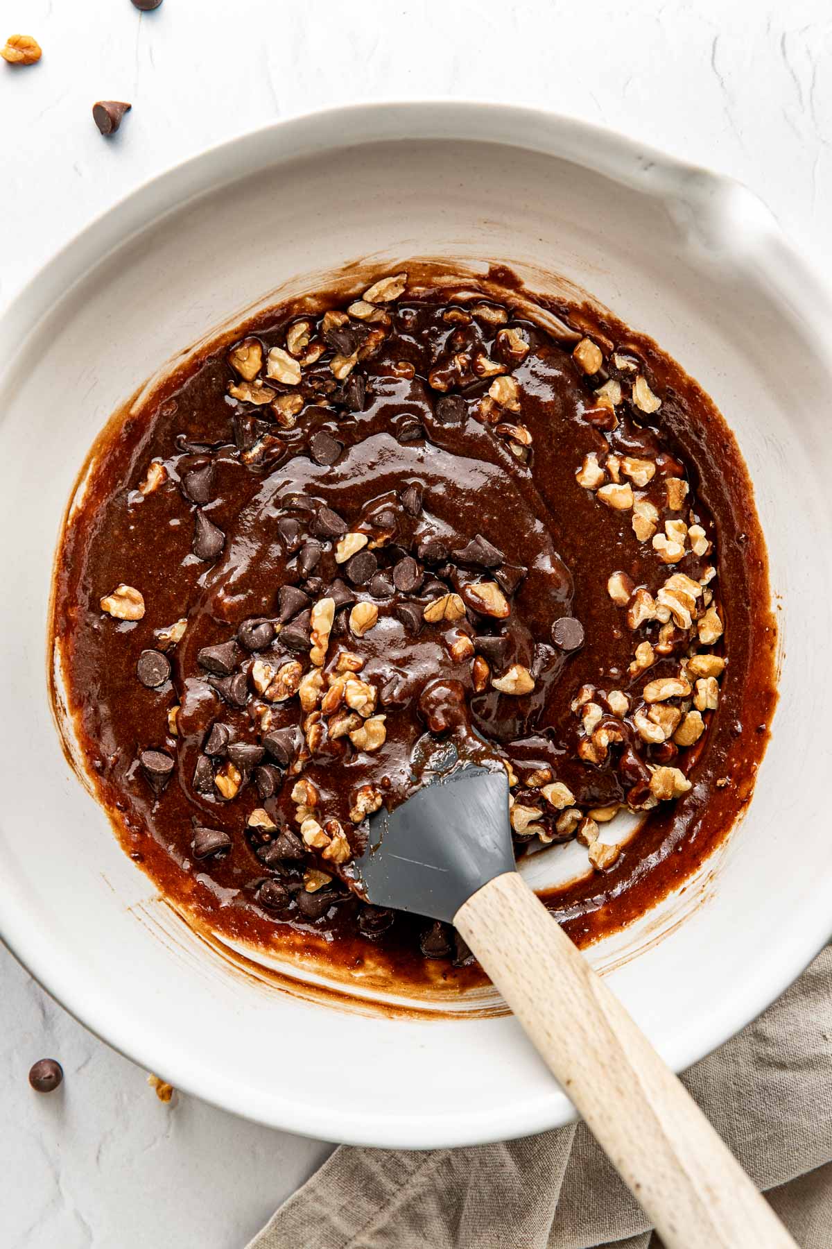 Overhead view of a white bowl filled with sweet potato brownie batter and a spatula stirring it. 
