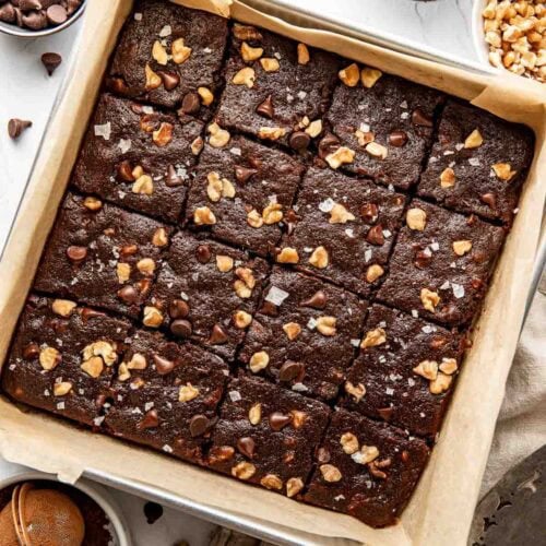 Overhead view of a parchment lined pan filled with freshly cut sweet potato brownies studded with nuts and chocolate chips and sprinkled with flakey sea salt.