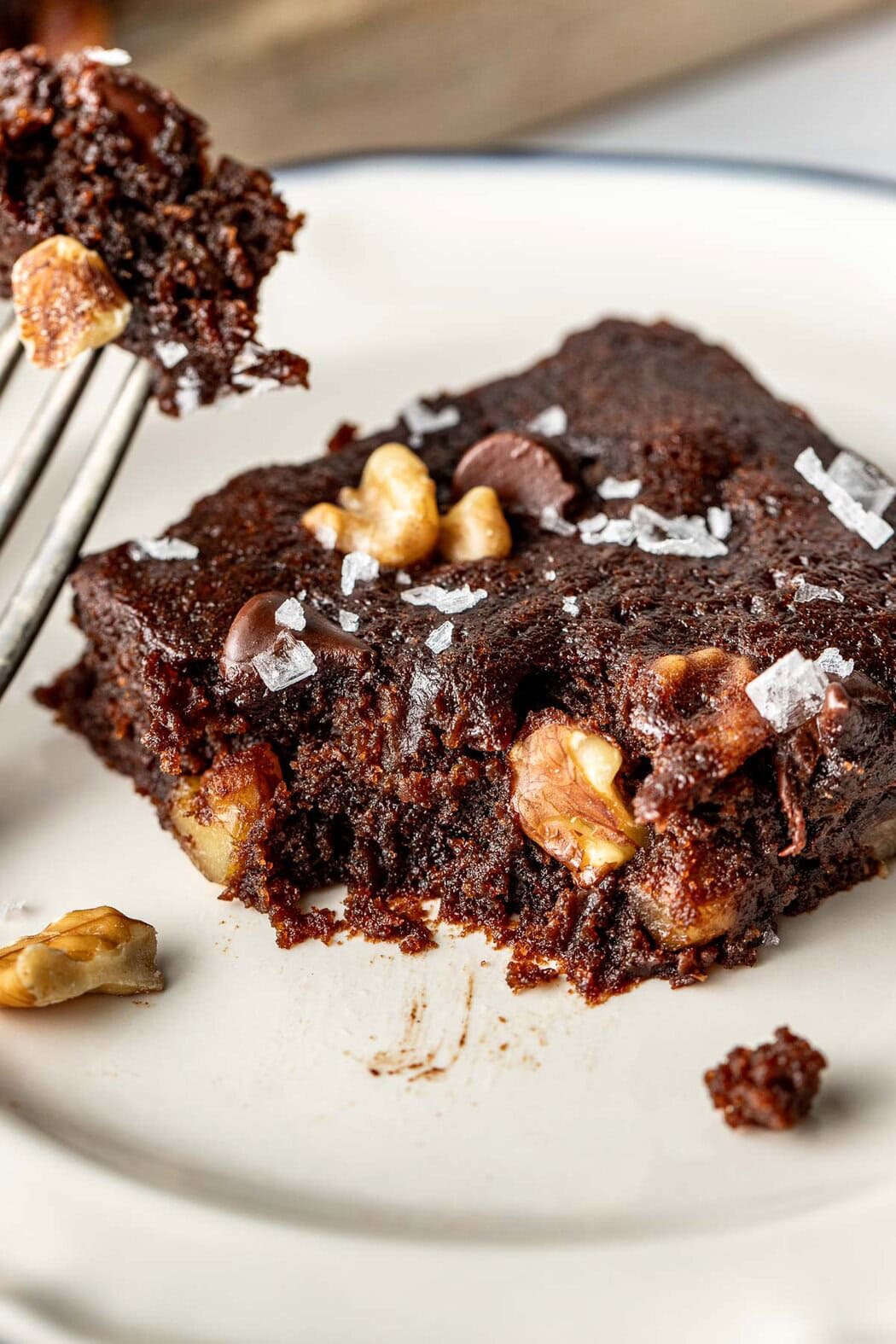 Close up view of a fork removing a bite from a pumpkin brownie to see the fudgy inside and pieces of nuts and chocolate chips. 