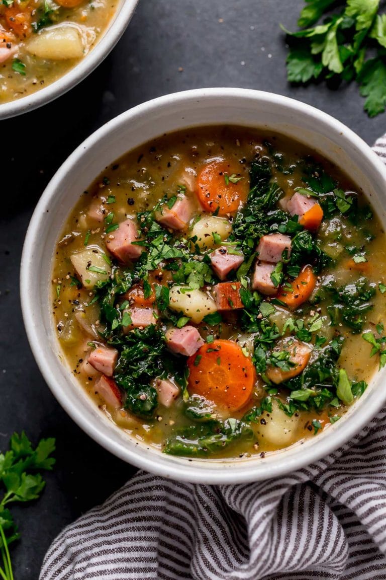 Overhead view of a bowl of creamy ham and potato soup topped with black pepper. 