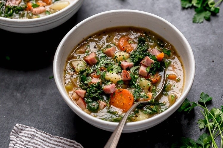 Close up view of a bowl of ham and potato soup topped with black pepper.