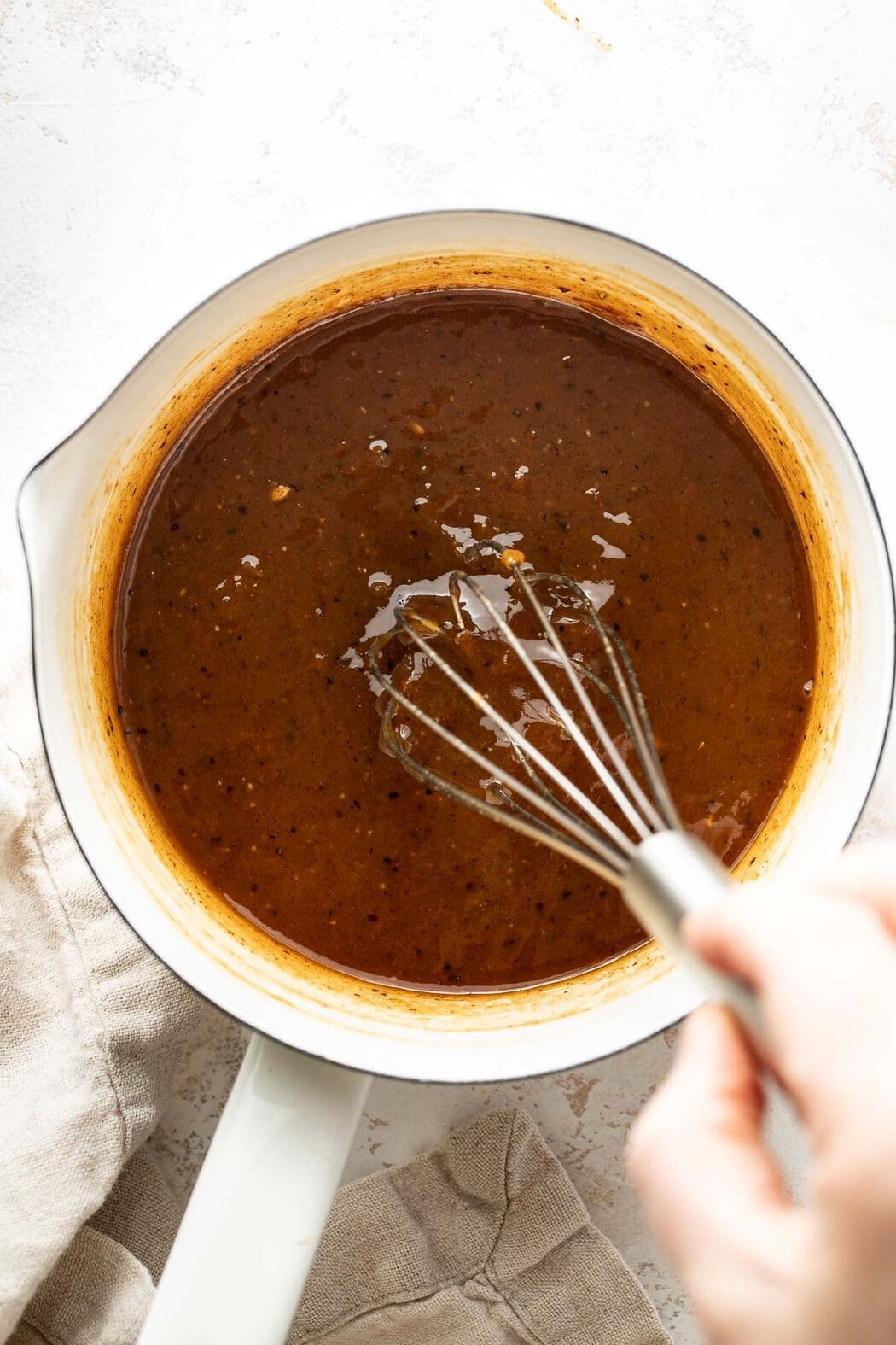 Overhead view of a small saucepan filled with ham glaze and whisk stuck into the sauce.