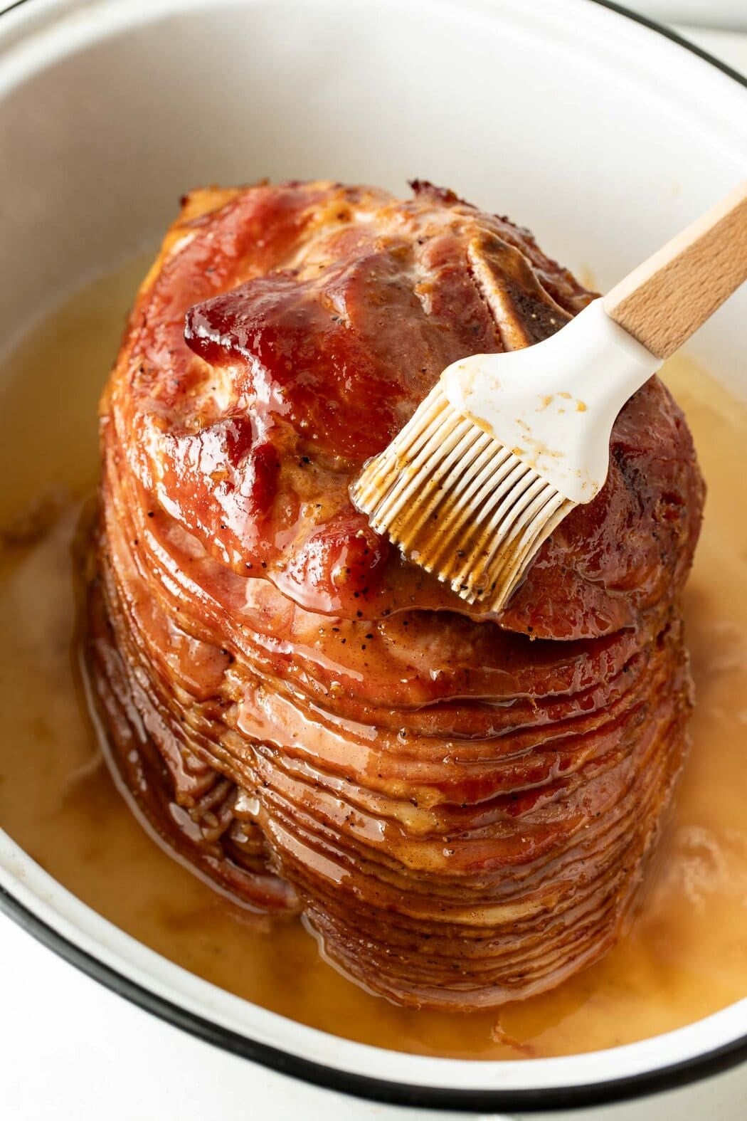 Closeup view of a spiral cut ham with a brush spreading glaze over the top.