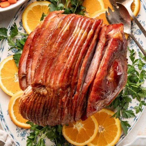 Overhead view of a spiral cut ham with a glaze over the top surrounded by sliced oranges.