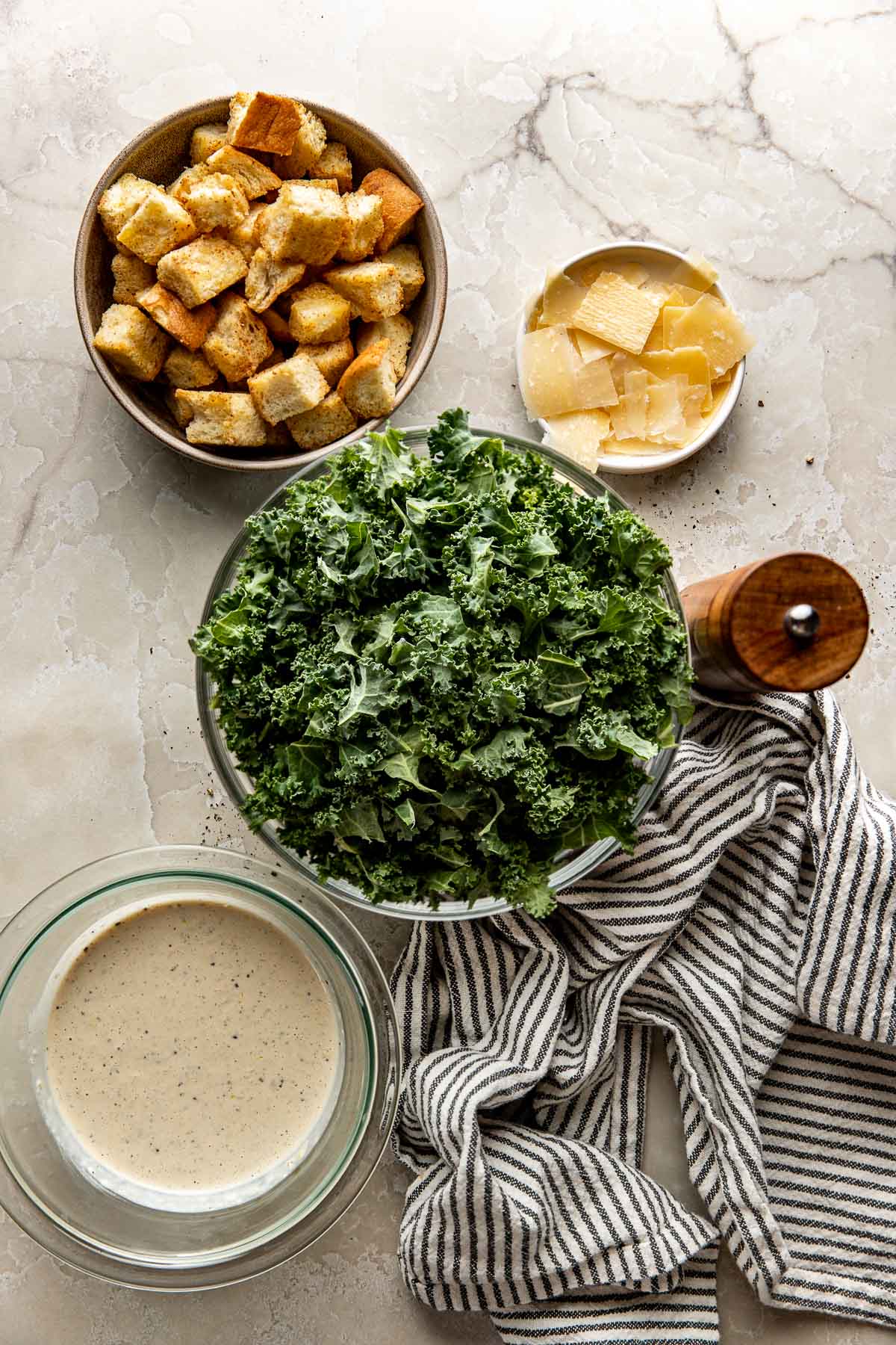 Overhead view of a variety of ingredients for Kale Caesar Salad in different sized bowls.