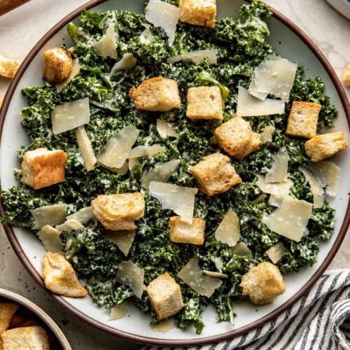 A plate of Kale Caesar Salad topped with croutons and shaved parmesan cheese