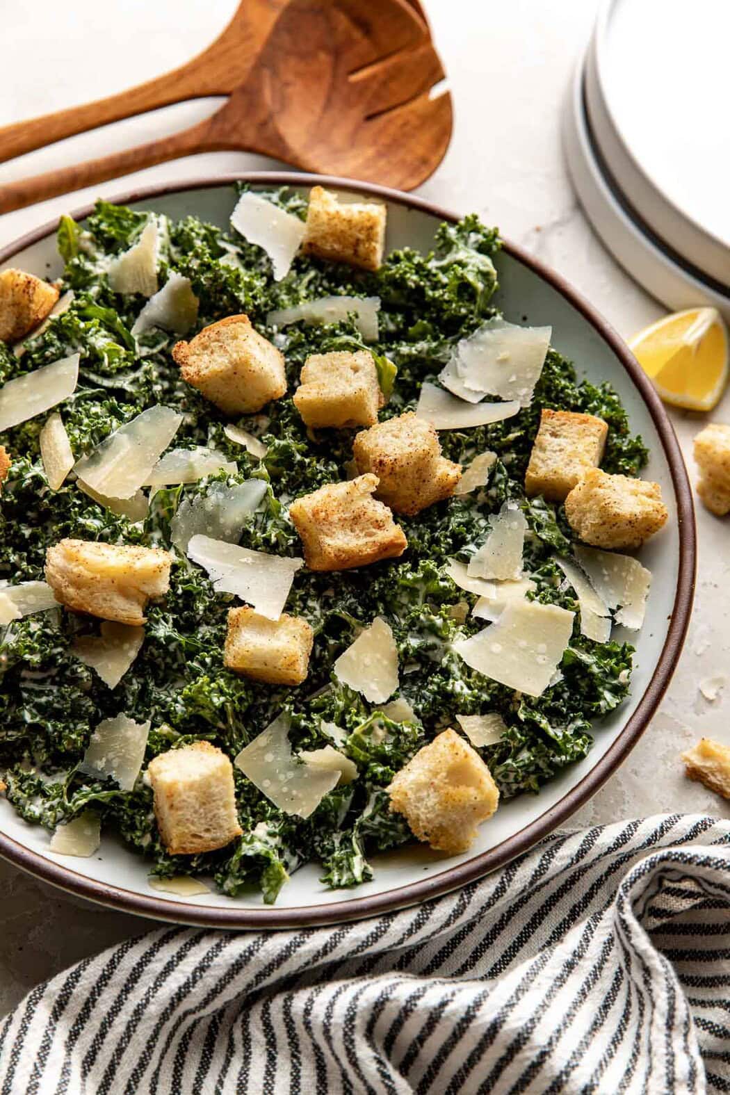 Close up view of a plate of Kale Caesar Salad topped with shaved parmesan cheese and crispy homemade croutons. 