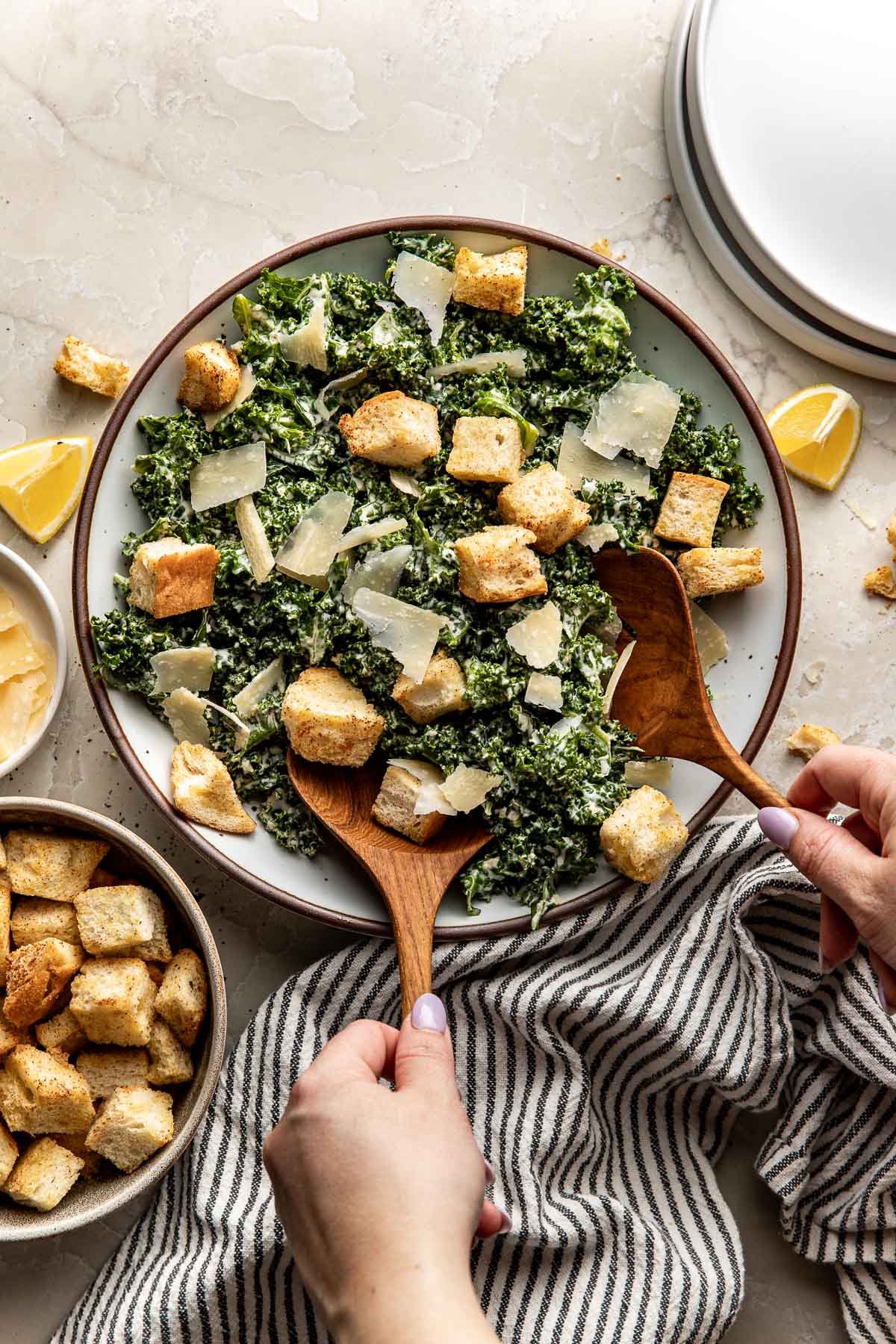 two hands tossing a fresh Kale Caesar Salad with wooden spoons