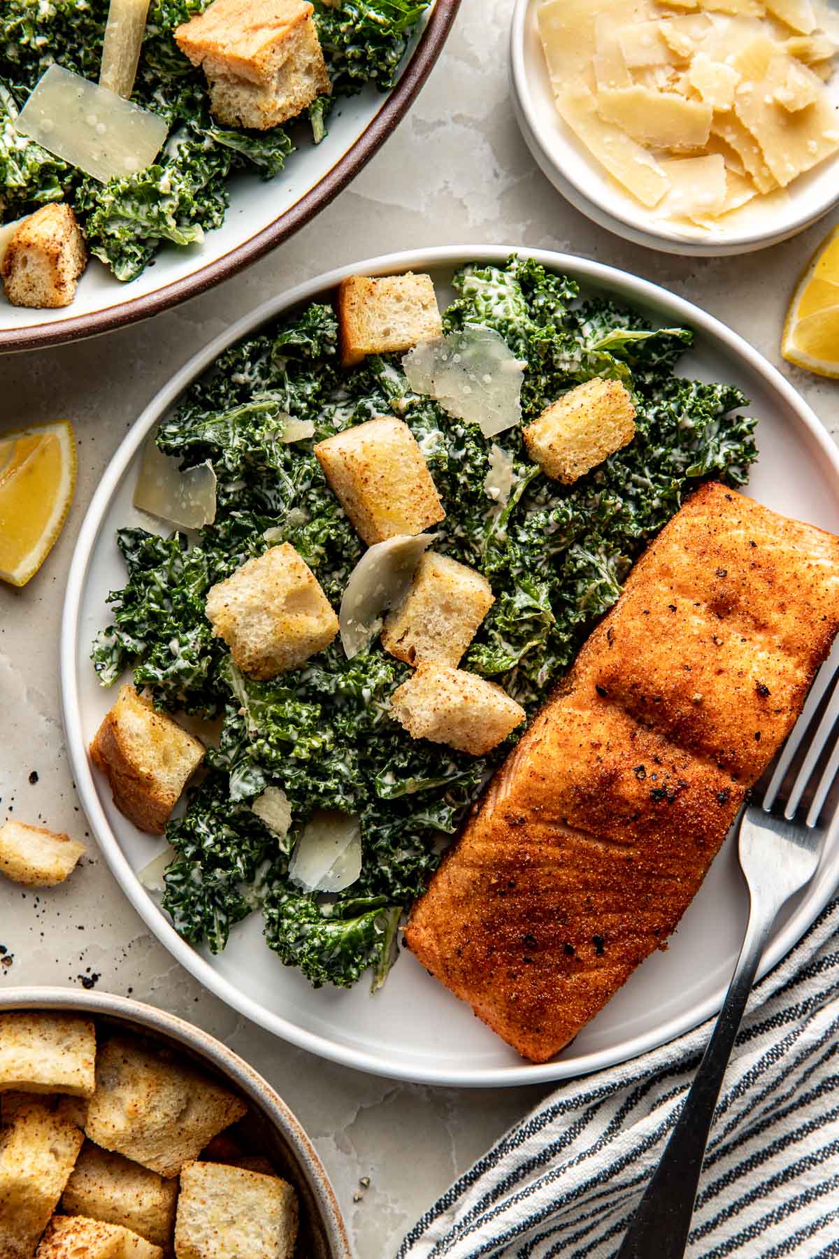 Overhead view of a plate of a fresh Kale Caesar Salad with a salmon fillet on the side