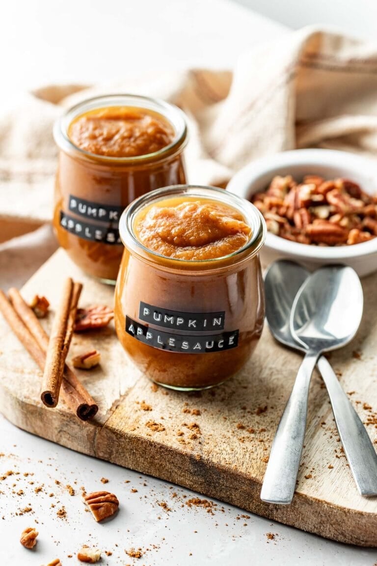 A wooden cutting board filled with glass jars of pumpkin applesauce