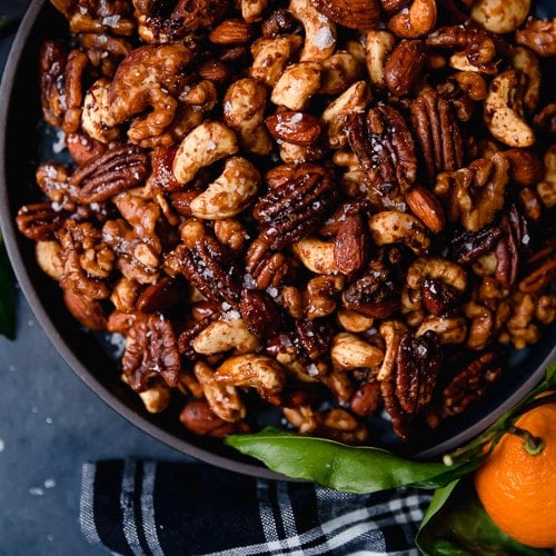 Overhead view of a black bowl on a dark grey surface filled with Slow Cooker Spiced Nuts (includes cashews, almonds, and pecans).