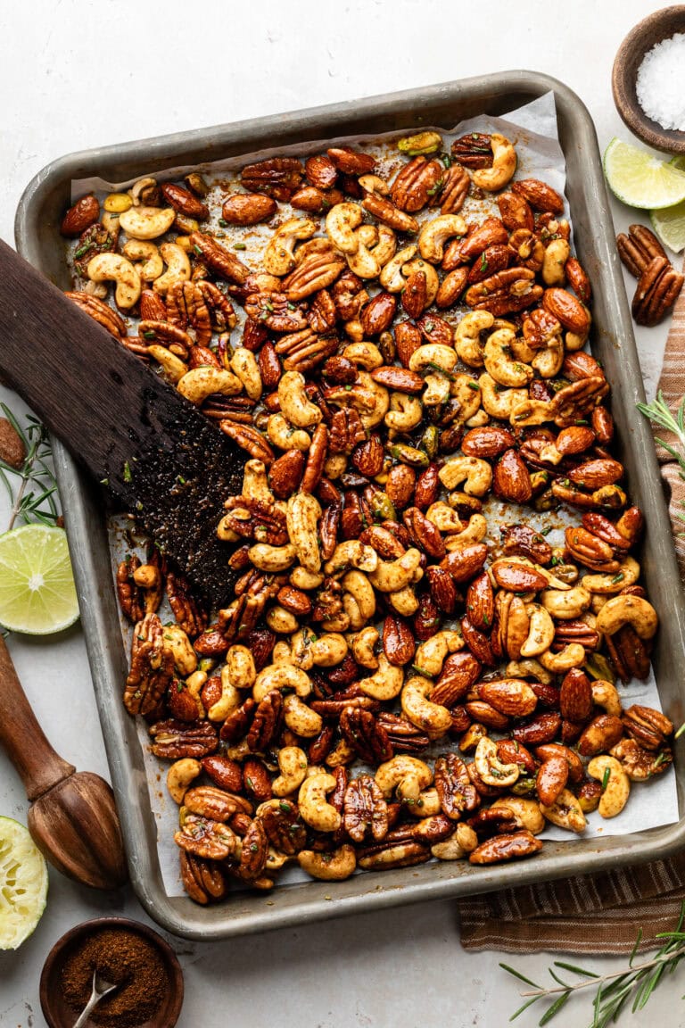Overhead view of a sheet pan filled with roasted nuts topped with seasonings.
