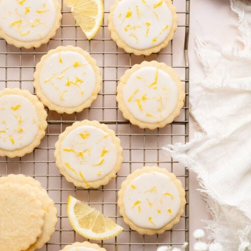 Overhead view of a cooling rack filled with lemon cookies with lemon wedges arranged around them.
