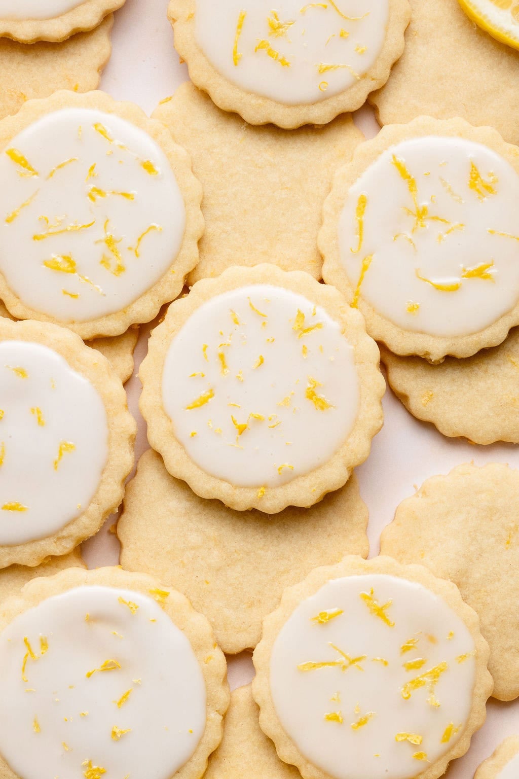 Overhead view of a variety of lemon frosted cookies arranged on a white countertop and sprinkled with lemon zest. 