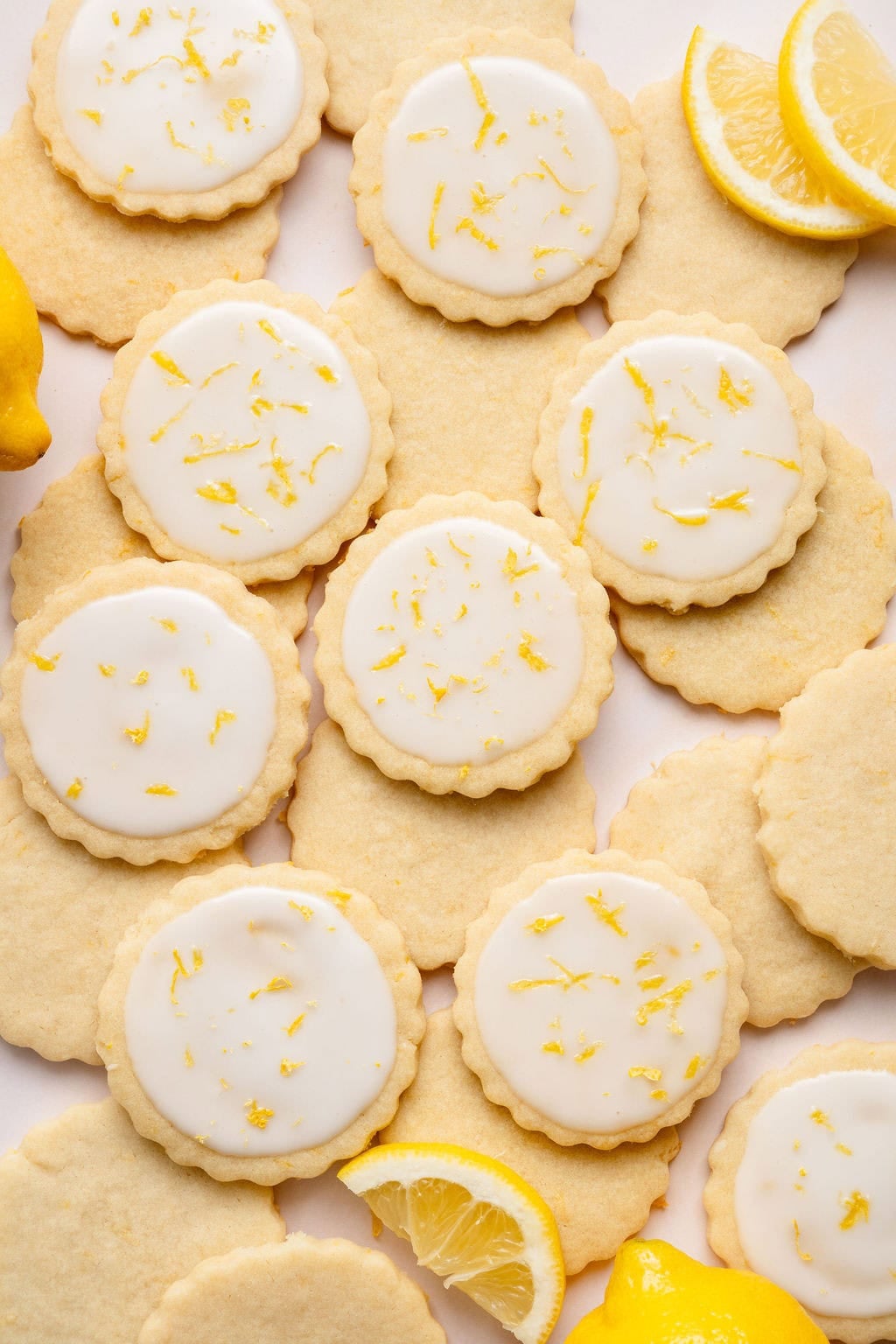 Overhead view of a variety of lemon cookies arranged on a white countertop sprinkled with lemon zest. 