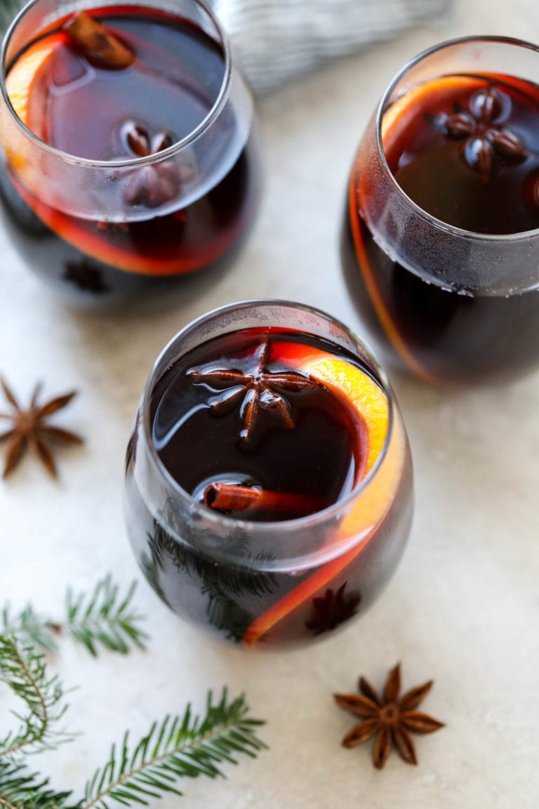 Overhead view of three glasses of mulled wine topped with star anise and an orange peel.