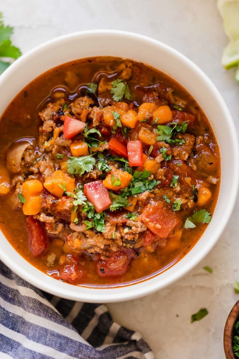 Overhead view of a bowl filled with turkey chili with bright sweet potatoes and tomatoes and topped with fresh cilantro. 