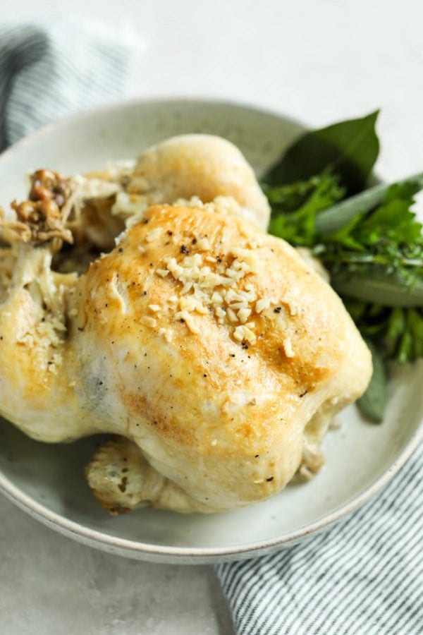 Overhead view of a cooked whole chicken in an off-white bowl on a pin-striped napkin. 