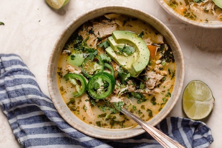 An overhead view of slow cooker white chicken chili in a cream bowl and topped with jalapeno and avocado slices.