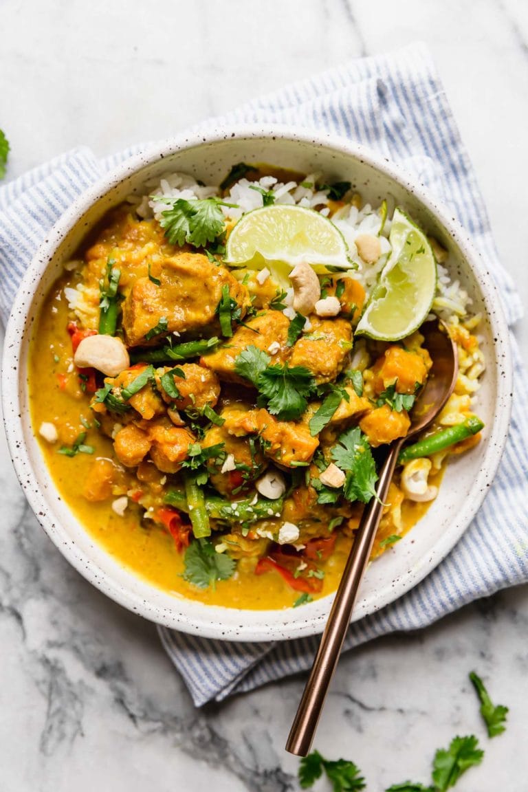Overhead view of a bowl of chicken sweet potato curry on top of rice and topped with fresh herbs and garnished with limes.