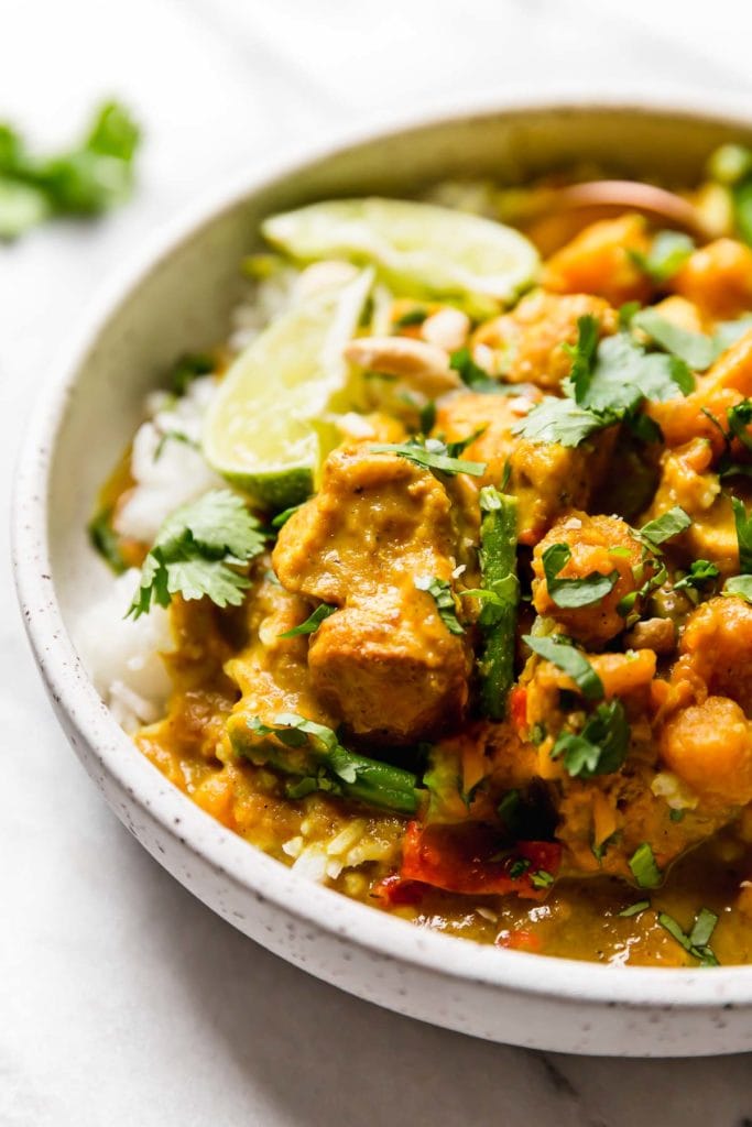 Creamy Chicken Curry with sweet potatoes topped with cilantro and lime wedges in a speckled bowl