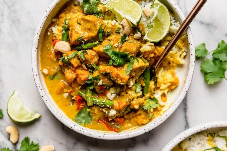 Close up overhead view chicken sweet potato curry topped with cilantro and lime wedges.