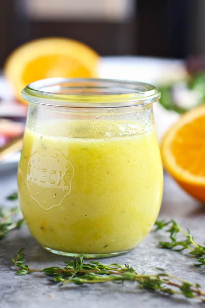 A glass weck jar of Citrus Vinaigrette with Thyme and citrus fruit in the background