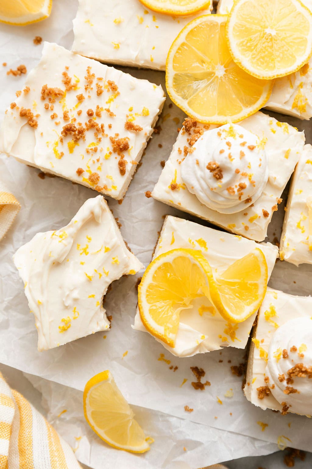 Overhead view of No Bake Lemon Cheesecake Bars cut into squares and topped with lemon zest and lemon slices. 