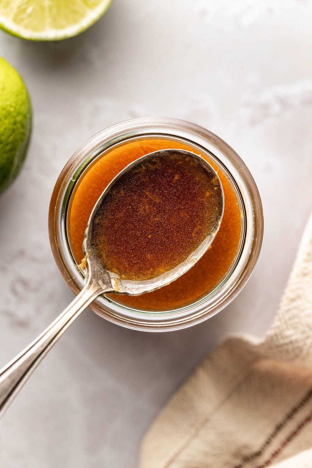 Overhead view of a glass jar filled with Sesame Ginger Dressing and a spoon showing the consistency and rich amber color. 