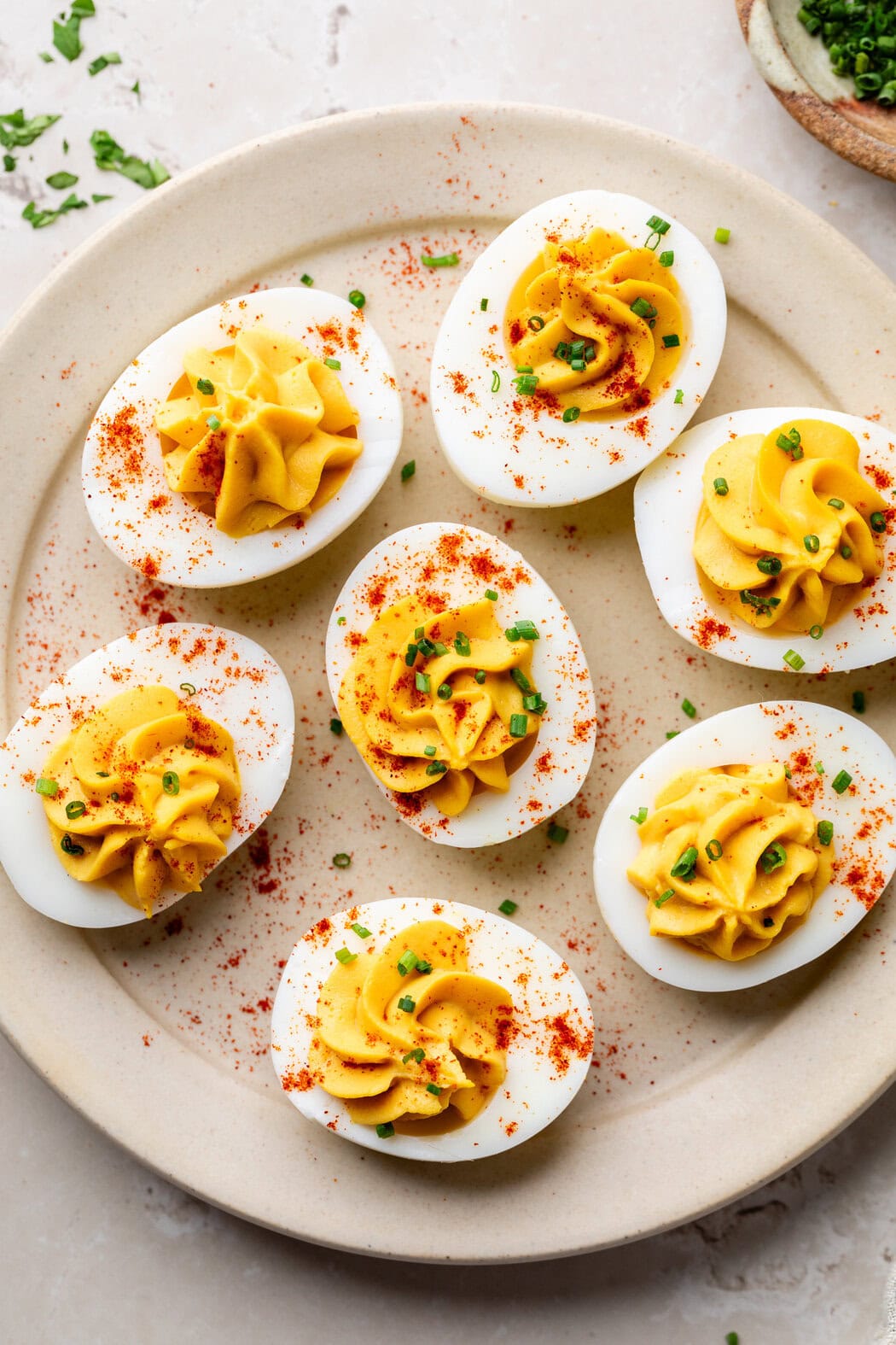 Overhead view of a plate of healthy deviled eggs topped with paprika and fresh chives. 