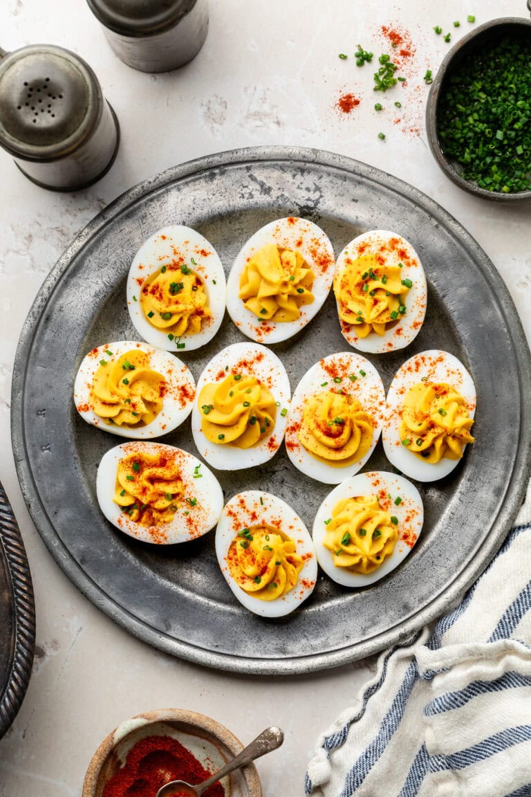 Overhead view of a platter filled with deviled eggs sprinkled with chives and paprika.