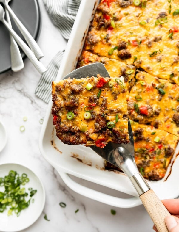 A serving spatula lifting a piece of sausage egg bake from a white casserole dish