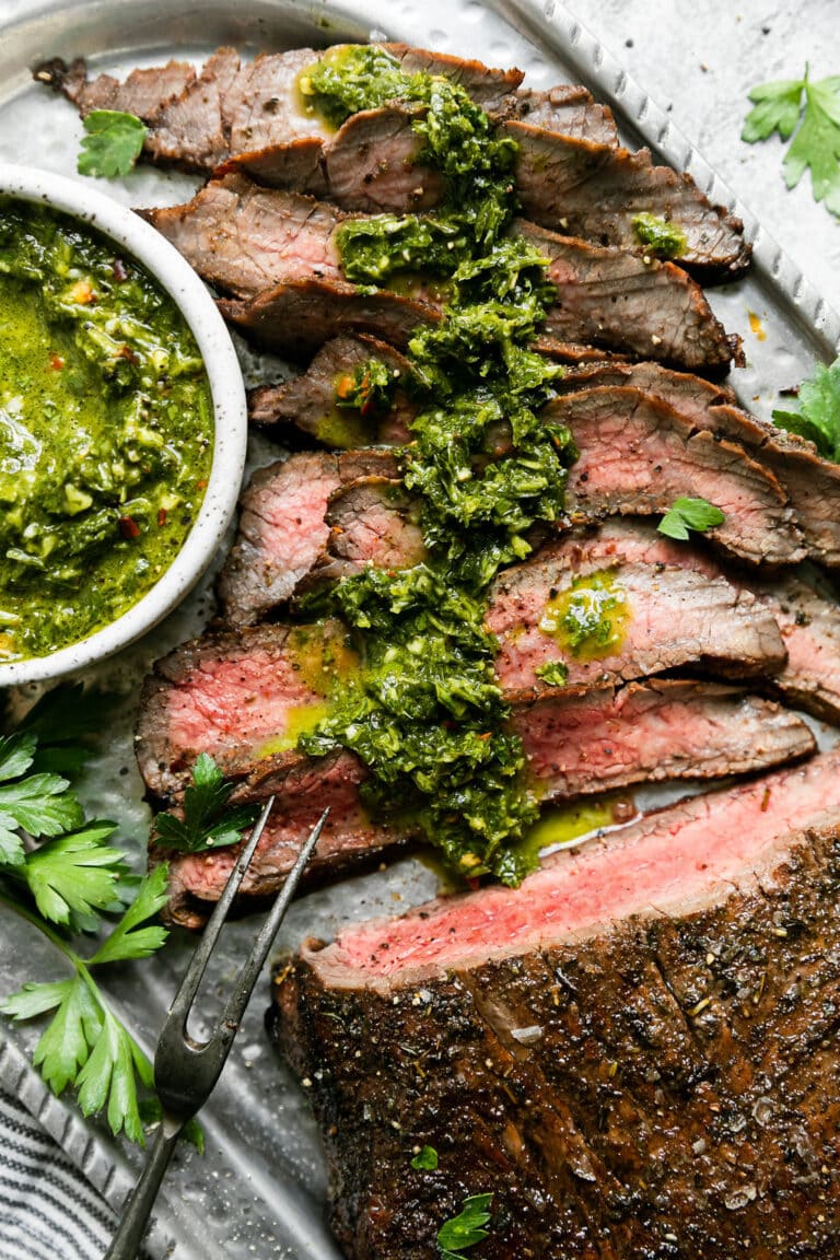 Overhead view of a sliced grilled flank steak topped with a green chimichurri sauce. 