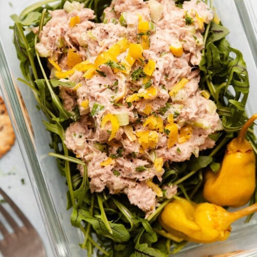 Overhead view of a glass meal prep container filled with arugula and topped with Tuna Salad.