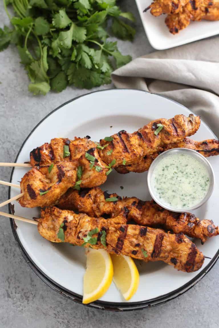 Overhead view of a plate of chicken tikka masala skewers topped with fresh herbs and garnished with lemon wedges.