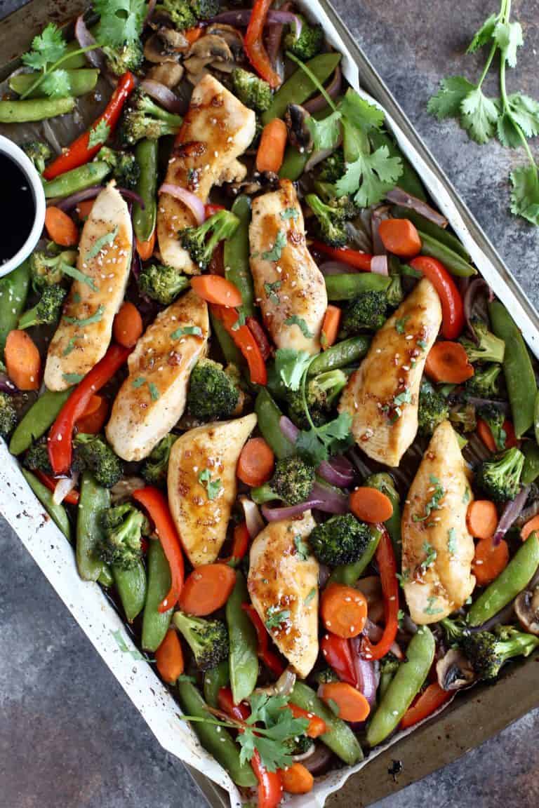 Overhead view of a sheet pan of teriyaki chicken and vegetables topped with sesame seeds. 