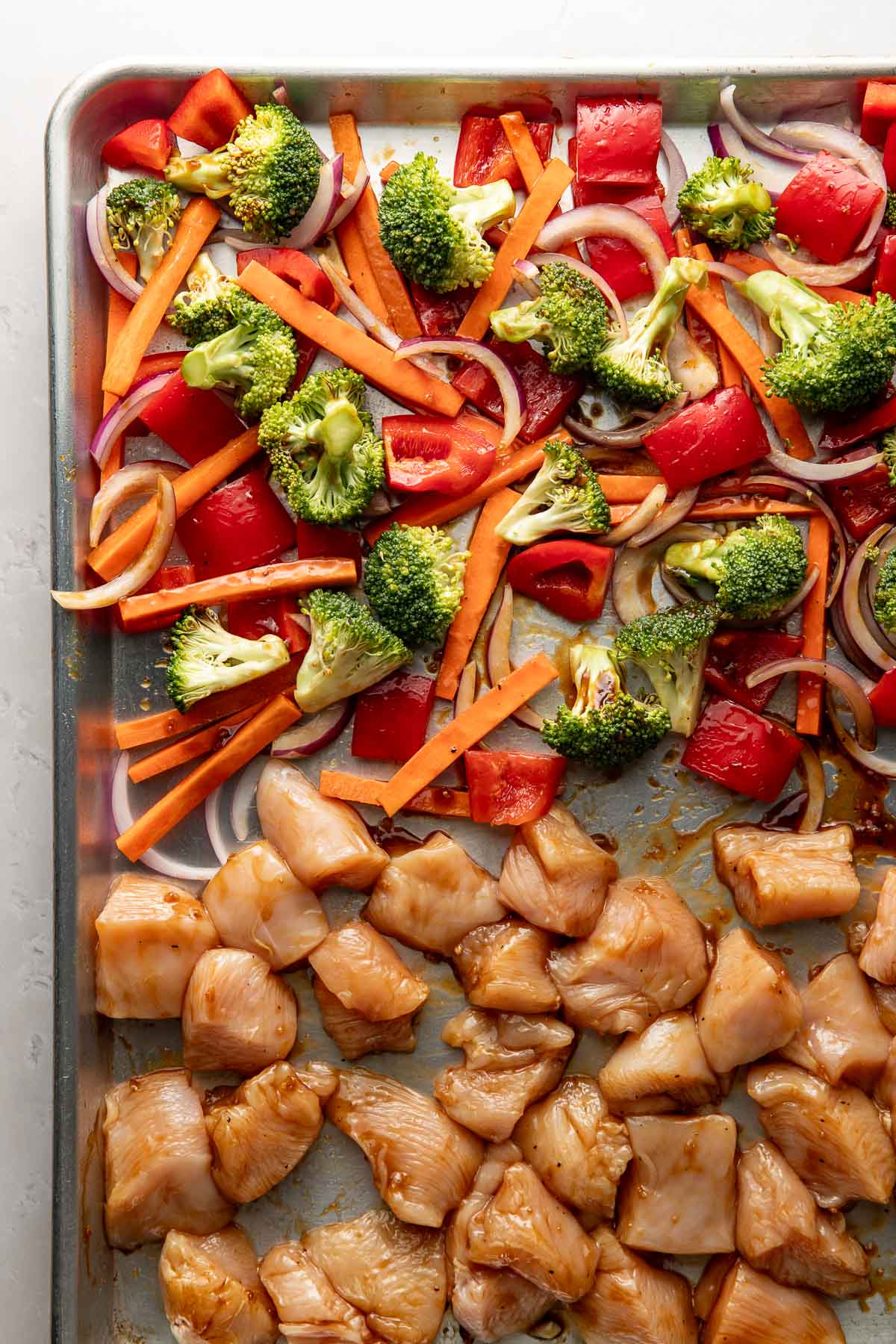 Raw chicken and vegetables tossed with teriyaki sauce on a sheet pan.