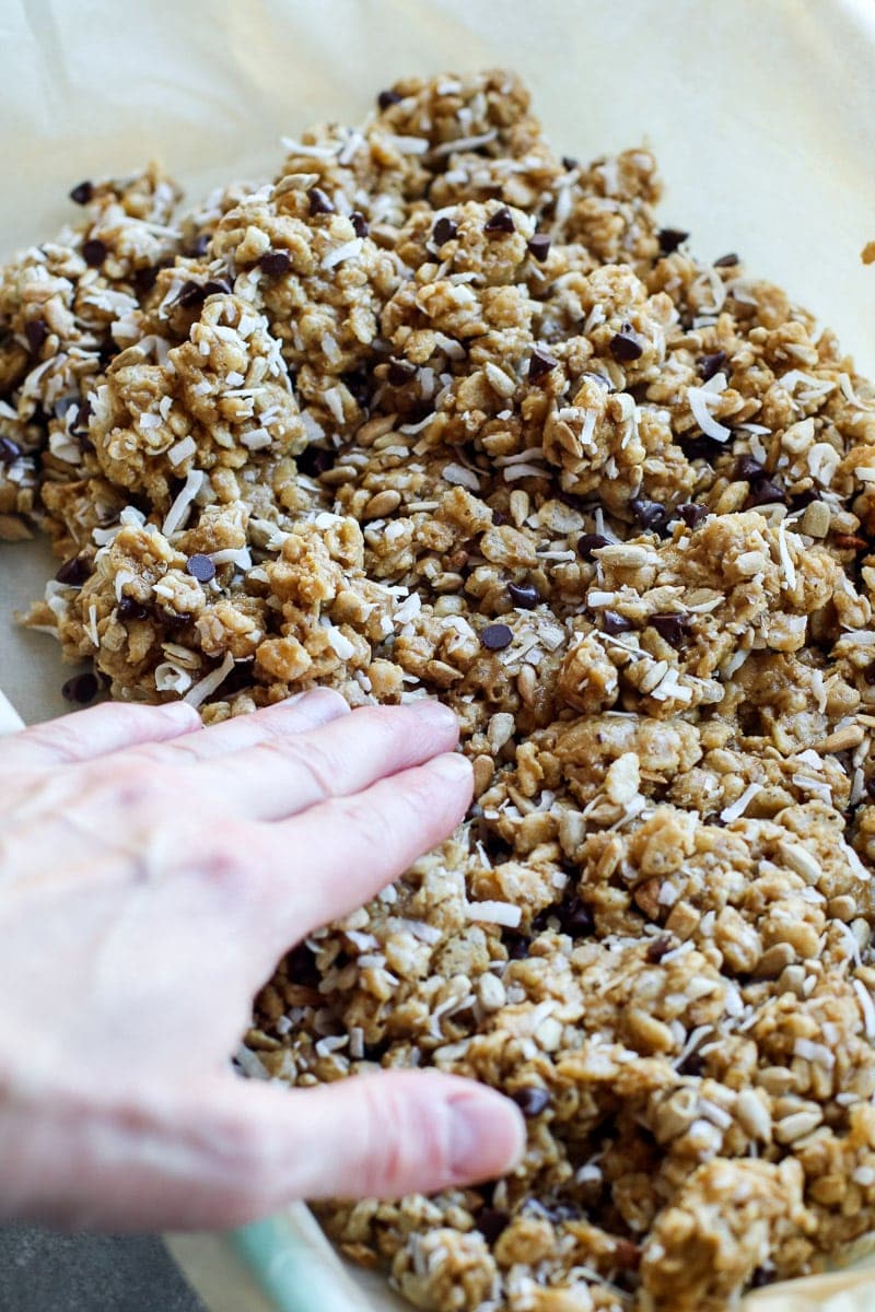 Homemade chocolate chip granola bars being pressed into a baking dish