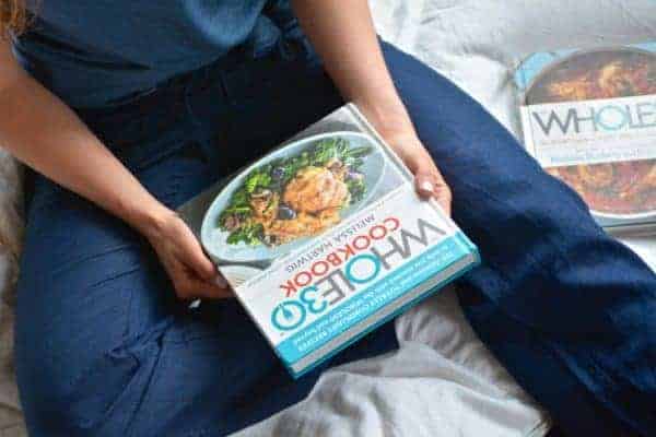 A woman holding a Whole30 cookbook on her lap