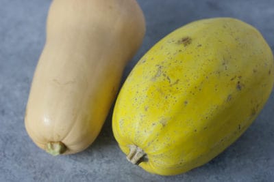 A spaghetti squash and a butternut squash laying side by side on a gray countertop.
