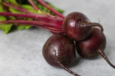 A group of beets with the roots and stems on them laying on a gray countertop.