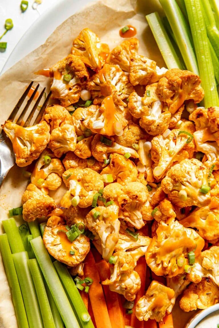 Overhead view of roasted buffalo cauliflower bites surrounded by fresh cut carrots and celery.